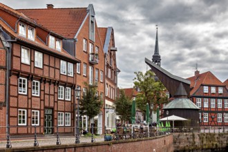 Half-timbered houses and a decorated tower on a riverbank with terraces and cloudy sky, The old
