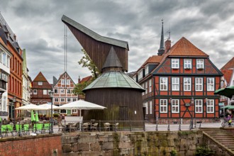 Historic timber crane building and half-timbered houses with terraces under a cloudy sky, The old