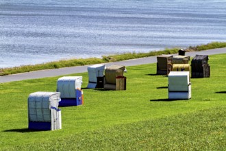 Beach chairs in different colors in a meadow next to a waterside road, beach chairs on the beach in