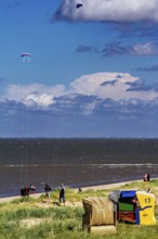 Beach chairs by the sea with people and kites in the sky under blue sky and clouds, beach chairs on
