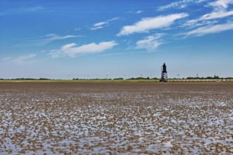 A lighthouse in the Wadden Sea with wind turbines on the horizon under a blue sky, Die Kugelbake