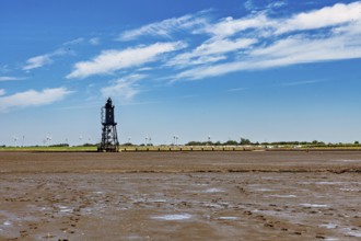 A lighthouse in the Wadden Sea with wind turbines in a vast, cloudy landscape, The Kugelbake von