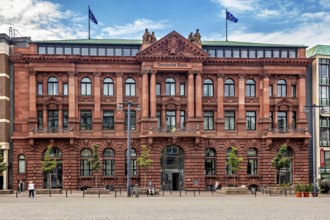 Historic bank building with red façade and two flags on the roof under a blue sky, The center of