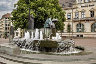 Fountain with horse sculptures and running water on a town square in front of a historic building,