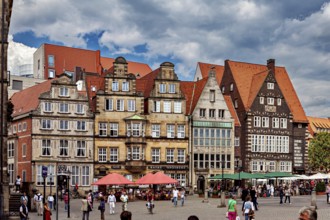 Half-timbered houses in a historic old town. People stroll across a busy market square in cloudy