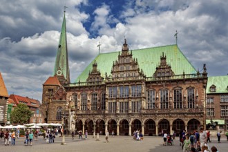 Large Renaissance building next to church tower, surrounded by people in a busy square under cloudy