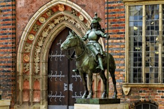 An equestrian statue in front of a Gothic building with richly decorated archway and red bricks,