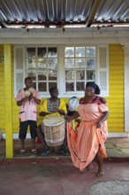 Guatemalan woman in traditional dress singing and dancing, men playing music in the back, Garifuna