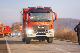 A fire truck drives on a road through a wooded area with emergency personnel, fire brigade exercise