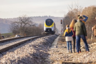 People watch a train traveling on a railway line in rural surroundings, fire brigade exercise at