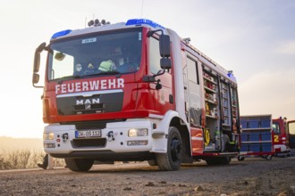 A fire engine with an open equipment door on a street in the morning light, ready to be deployed,