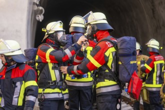 Firefighters in protective clothing deployed in front of a tunnel, focused on communication tasks,