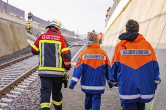 Firefighters in blue and orange uniforms walk along a railway line, fire department practice at the