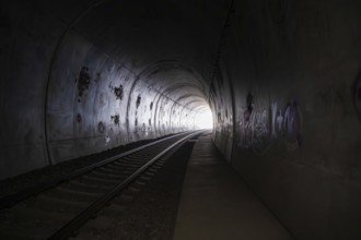 Dark tunnel with railroad tracks, graffiti and a light in the distance, fire brigade exercise on
