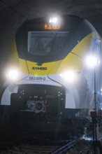 Yellow train travels through an illuminated tunnel on dark tracks, fire department exercise on the