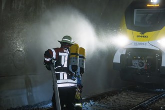 Firefighter with hose and respirator in front of a train in a tunnel, fire department exercise on