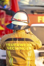 A firefighter stands in front of a fire truck wearing protective clothing, fire department exercise