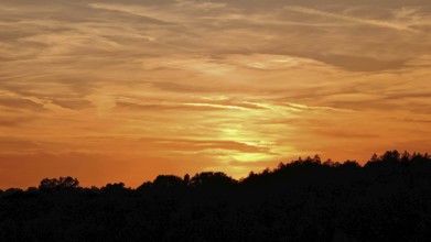 Orange sunset with silhouettes of trees and soft sky, Frankenwald nature park Park