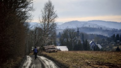Rural trail leads to a small village with a church in the background, surrounded by hills,