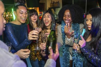 Group of excited diverse young adult friends smiling and laughing while celebrating a special