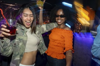 Diverse young women are having fun, raising drinks, and dancing together in a lively nightclub
