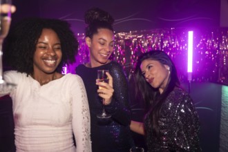 Three diverse women friends enjoying a night out, toasting with champagne and smiling while