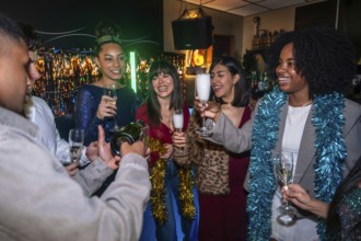 Diverse friends celebrating indoors with festive decorations as one man pours champagne into