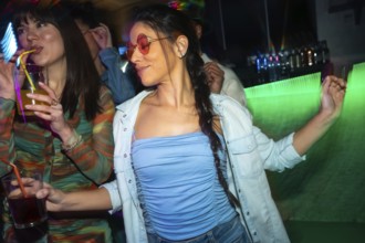 Young women enjoying nightlife, dancing and drinking cocktails with neon light reflections at a