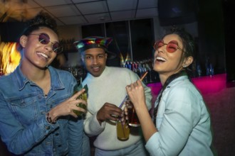 Diverse group of young people socializing at a bar, laughing and holding cocktails under colorful
