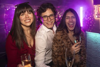 Three diverse young friends celebrating and having fun together at a vibrant nightclub, holding