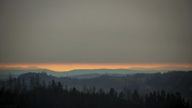 Forest and mountains at dusk below a cloudy horizon, with Staffelberg on a glowing horizon,