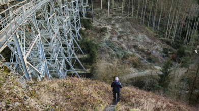 Hikers on a path next to a large metal-textured bridge, old railroad bridge in the forest,