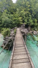 Wooden suspension bridge over green-turquoise water, surrounded by thick forest, Soca Valley,