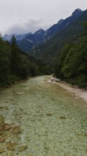 Long river with gravel bed surrounded by wooded mountains under a cloudy sky, Soca Valley, Slovenia