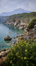 Rocky coast with turquoise water and a snow-capped mountain Tahtali Dagi in the background,