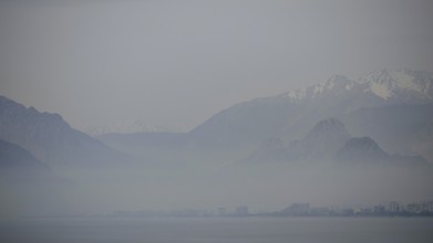 Blurred mountains rise above the misty sea under a grey sky, Antalya, Turkey