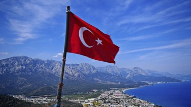 Turkish flag flies over a coastal town with mountains and blue sky, Kemer, Turkey