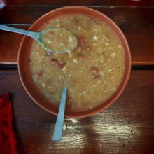 A plate of stew on a wooden table with a spoon lying next to it, Slovenia