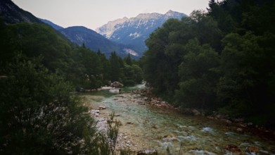 A mountain river flows through a wooded landscape with mountains in the background, Soca Valley,