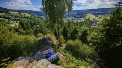 A panorama from a viewpoint with a person on a bench with a view of a picturesque valley,