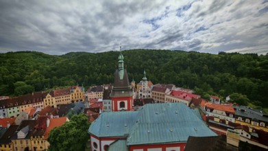 City view with church tower and historic buildings in front of wooded hills, view of Loket, Czech