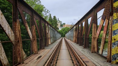 Old, rusty metal railroad bridge leads through green forests to a remote small town, Loket, Czech