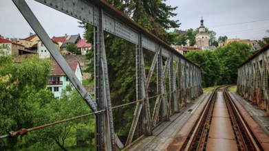 Metal railway bridge leads across a river to a small town with green surroundings, Loket, Czech