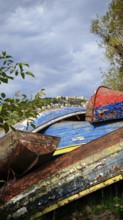 Weathered, colorful boats lie under a cloudy sky surrounded by trees and shrubs, Lake Ohrid, North