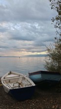 Two boats are lying on the shore of a calm lake under a cloudy evening sky, Lake Ohrid, North