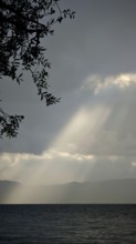 Dramatic ray of light falling through clouds onto a calm lake, Lake Ohrid, North Macedonia