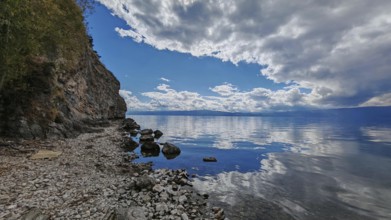 A peaceful rocky coast with a lake whose water reflects the clouds of the dramatic sky, Lake Ohrid,