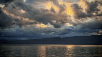 Dramatic clouds and golden light are reflected in the calm water of the lake during a sunset, Lake