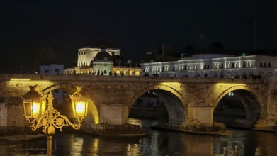 Illuminated bridge at night over a river with historic architecture, Skopje, North Macedonia