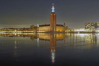 Night scene of a town hall with illuminated tower, peaceful reflection on calm water, Nobel Prize,